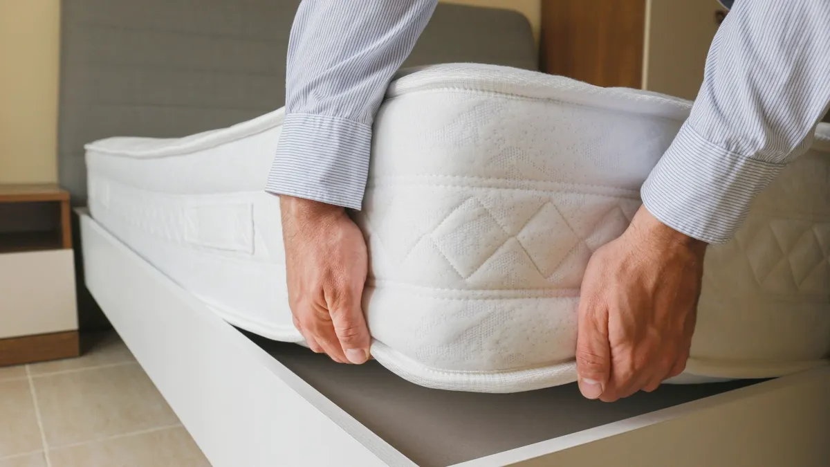 Two people rotating a mattress 180 degrees on a bed frame