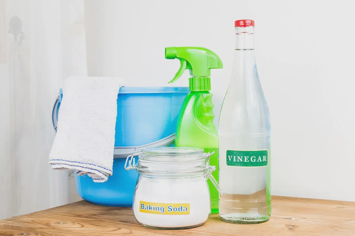 Baking soda, mild dish soap, white vinegar, and microfiber cloths laid out on a wooden surface