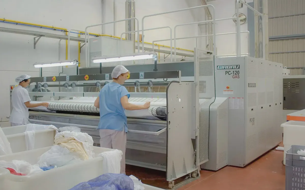 Industrial flatwork ironer pressing hotel sheets through heated rollers
