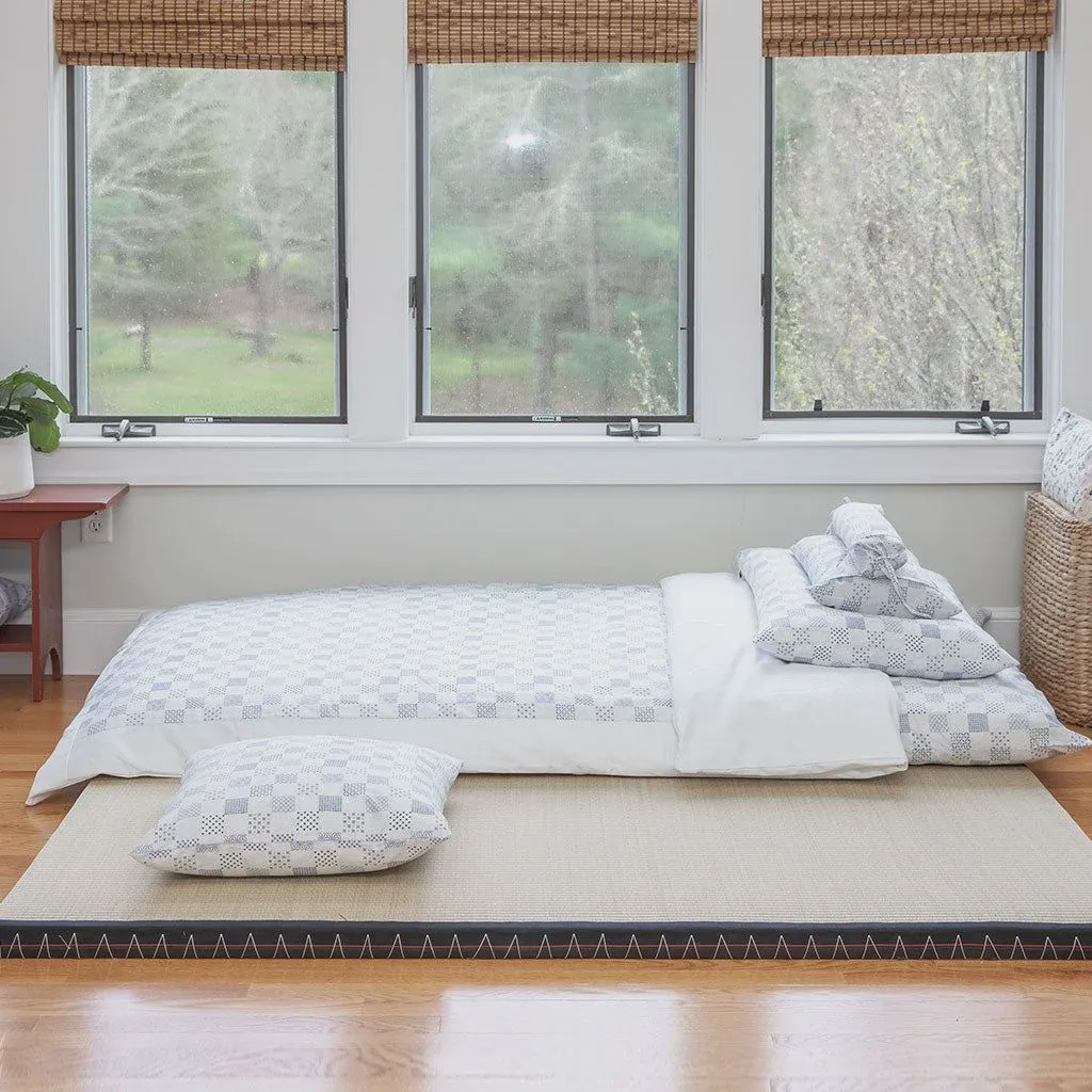 Traditional Japanese shiki futon rolled on a tatami floor, showing the thinner traditional dimensions